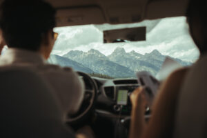 A couple drives through GTNP with a view of the Tetons through the front car window.